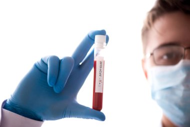 Test tüpü erkek elinde, doktor maskesinde kırmızı sıvıyla bir şişe tutuyor. Kan örneği kavramı, koronavirüs teşhisi, tıbbi araştırma.