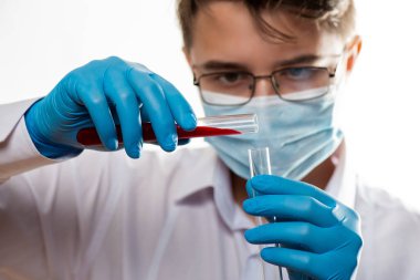 Test tüpü erkek elinde, doktor maskesinde kırmızı sıvıyla bir şişe tutuyor. Kan örneği kavramı, koronavirüs teşhisi, tıbbi araştırma.