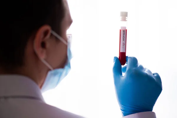 Test tube in male hand close up, doctor in medical mask holding a vial with red liquid. Concept of blood sample, coronavirus diagnostic, medical research.