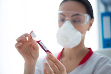 Maskeli kadın doktor, elinde kan örneğiyle bir şişe. Laboratuvar araştırması ve Covid-19 Coronavirus Tespit.