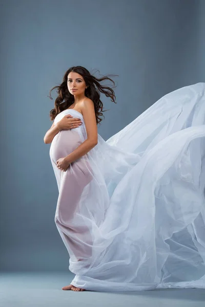 工作室的画像是穿着灰色背景的白色飞行服装面料的裸体孕妇 美丽健康的怀孕 快乐的母性 — 图库照片