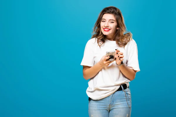 Девушка с телефоном в руках улыбается, изолированная на синем фоне — стоковое фото