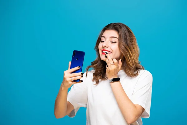 Girl Phone Her Hands Smiles Does Makeup Isolated Blue Background — Stock Photo, Image