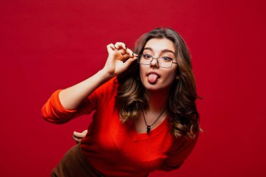 Genç otantik karizmatik kadın kırmızı duvara karşı komik ve dost canlısı bir dil uzatıyor. Bayan öğrenci bayan patron..