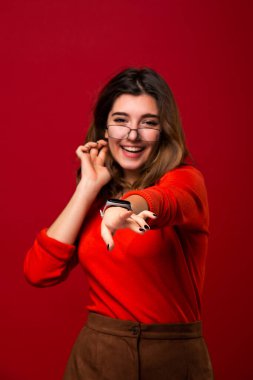 Kendinden emin gülümseyen kız öğrenci ya da gözlüklü iş kadını motivasyon sağlar ve başarı için para alır. Kırmızı arkaplanda izole.