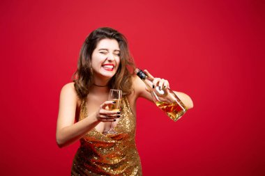 Kırmızı rujlu, altın rengi elbiseli ve elinde şampanya olan seksi bir kadın. Yeni yıl tatili kavramı, doğum günü partisi.