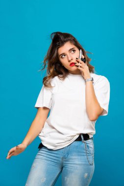 Genç ve güzel bir kız öğrenci cep telefonuyla konuşuyor. Mobil konuşma, iletişim. Mavi bir arkaplanda izole edilmiş.