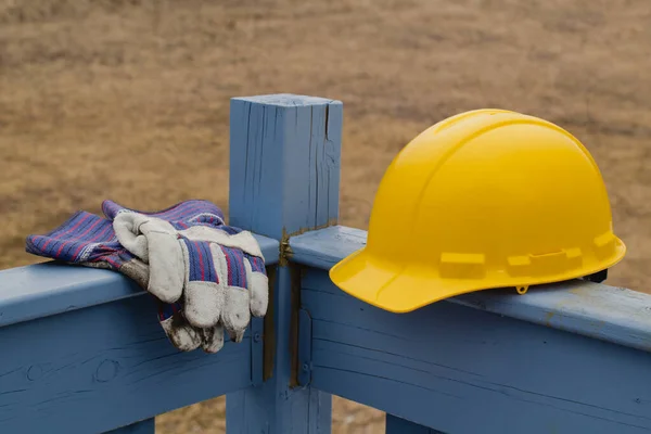 Yellow hard hat and work gloves on outdoor wooden railing