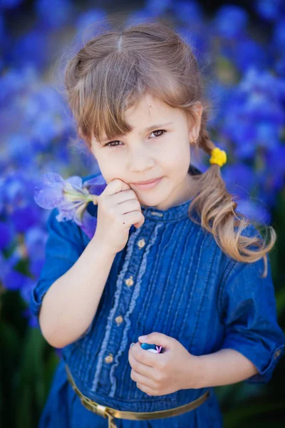Little girl in jeans dress with irises in hands — Stock Photo, Image