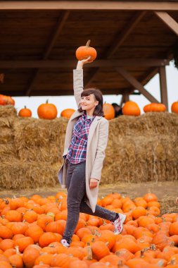 Balkabağı çiftliğinde bej ceketli bir kadın. Turuncu sonbahar ılık havasında.