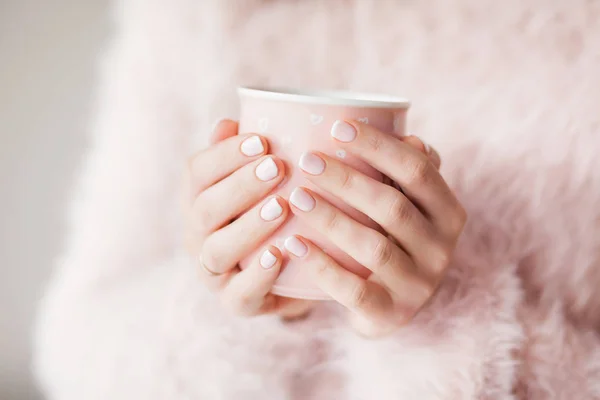 Ellerinde bir fincan, pembe kabarık kazaklı bir kız elinde pembe bir kupa tutuyor güzel manikürlü, sabah kahveli.