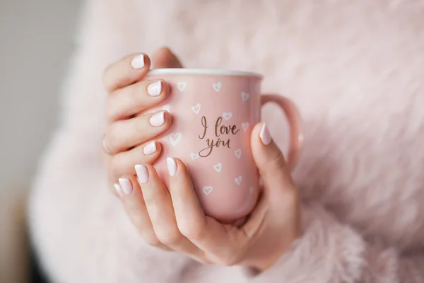 a cup in hands, a girl in a pink fluffy sweater holds a pink cup in her hands with beautiful manicure, morning coffee