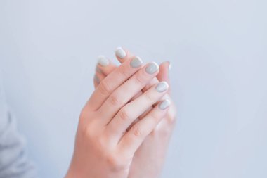 Gri arka planda gri manikürlü kadın elleri, arka planda avuç içi...