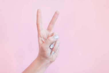 Hassas pembe arka planda gri manikürlü kadın elleri, sol elle gösterilen işaret.