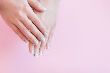 Kadın elleri narin pembe arka planda gri manikürlü, arka planda avuç içi...