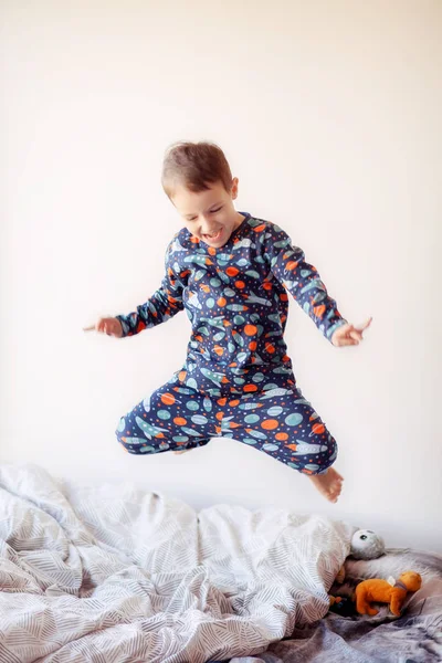 a boy in pajamas with space drawings jumps on the bed, morning exercises of the boy, good morning, the child woke up