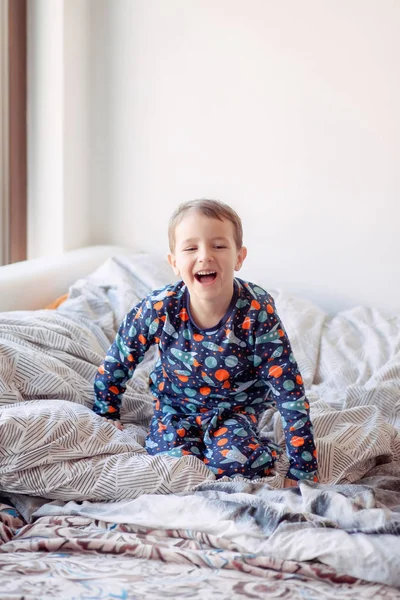 a boy in pajamas with space drawings jumps on the bed, morning exercises of the boy, good morning, the child woke up