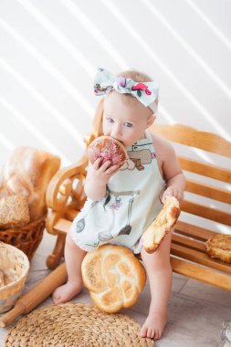 Bir yaşına kadar mutfak önlüğü takmış bir kız ve kafasında bir fiyonk bir bankta, rulolu turtaların yanında oturuyor, küçük bir fırıncı rulo ekmek yiyor.