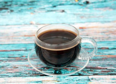 Mavi ahşap arka planda cam bir fincanda sade kahve.