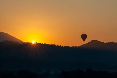 Sabah yükselen güneş ve sıcak hava balonu ovre dağında uçuyor. İnanılmaz sarı ve turuncu renklerle.