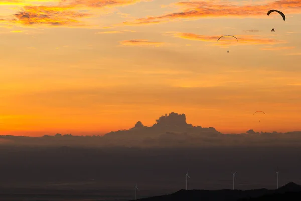 Landscape of Electric wind turbine generator at sunset on hill with dark clound and Powered Parachute Flying background