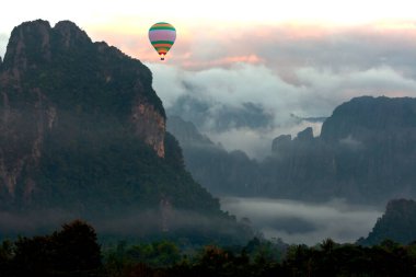 Renkli sıcak hava balonu gün doğumunda orman ve dağın üzerinde uçuyor.
