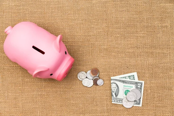 Pile of loose USD cash feeding a piggy bank — Stock Photo, Image