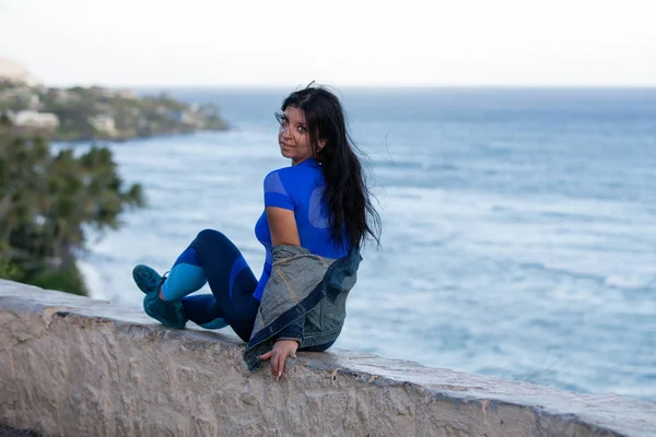Mulher sentada em uma parede acima do Oceano Pacífico — Fotografia de Stock