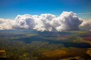 Mavi gökyüzü ve bulutlar ve dünya onların içinden bir uçak penceresinden görünür.