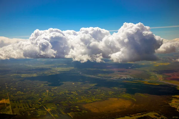 Mavi gökyüzü ve bulutlar ve dünya onların içinden bir uçak penceresinden görünür.