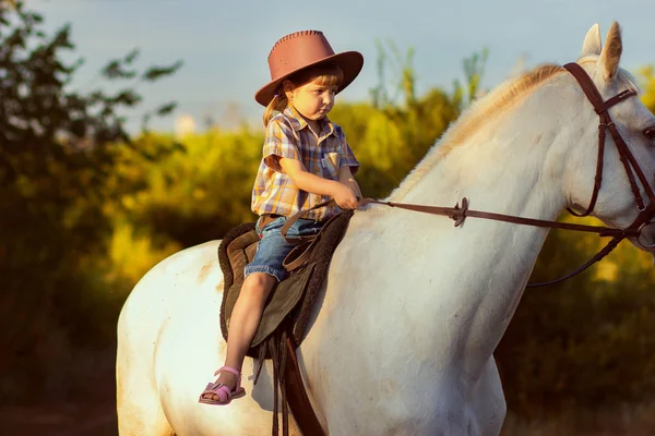 Het meisje in een hoed zit op een paard — Stockfoto