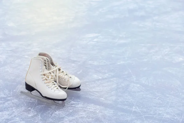 Un par de patines blancos de patinaje artístico se colocan en una pista de hielo en la esquina del marco — Foto de Stock