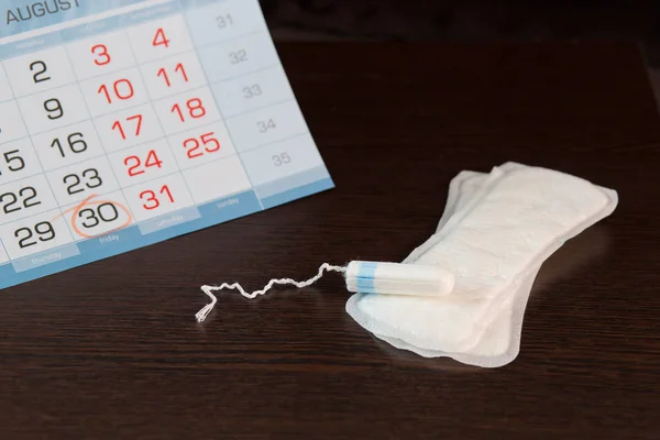 La almohadilla femenina diaria y el tampón están en el fondo del calendario, en el que se marca el día del comienzo del ciclo menstrual. —  Fotos de Stock