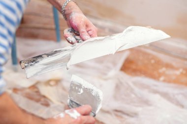 İşçi oturma odasındaki duvarları sıvamak için bir spatulaya macun koyuyor.