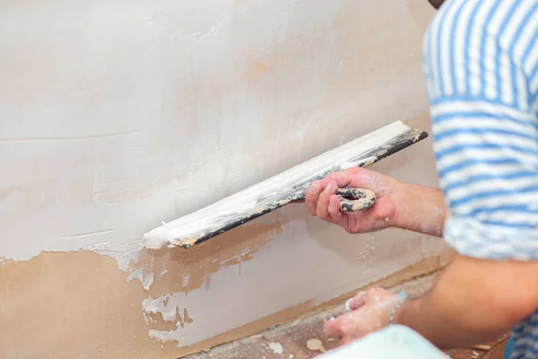 Trabalhador coloca massa de vidraceiro em uma espátula para rebocar paredes internas em uma sala de estar — Fotografia de Stock