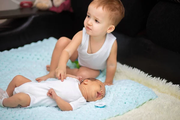 Um menino de dois anos aponta para seu irmão recém-nascido. Amizade de crianças na família — Fotografia de Stock