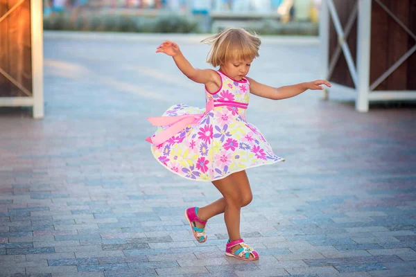 Uma menina em um vestido de verão dançando na rua na praça da cidade. A criança está girando e voando um sundress — Fotografia de Stock