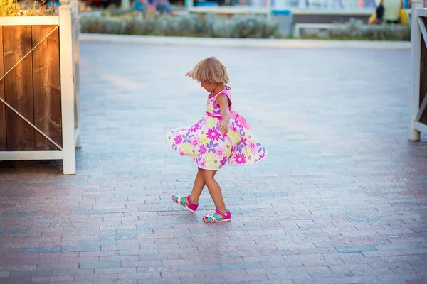 Uma menina em um vestido de verão dançando na rua na praça da cidade. A criança está girando e voando um sundress — Fotografia de Stock