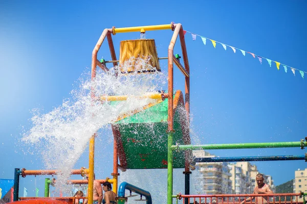 Egy vízzel teli vödör, ami kiömlik az emberekre egy vízi parkban. Nyári szórakozás a vízben — Stock Fotó
