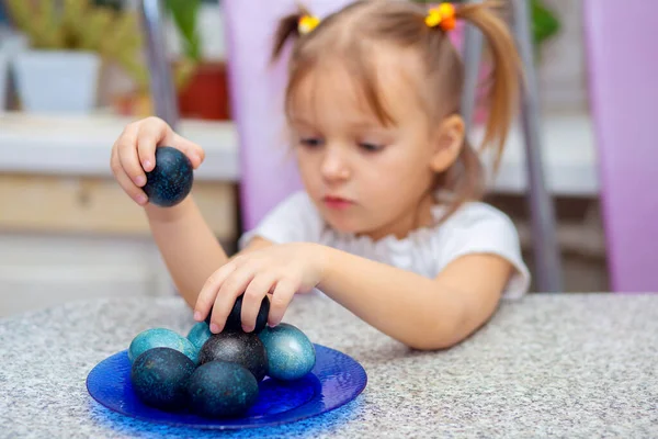 Pequena menina bonito joga na cozinha com ovos de Páscoa coloridos . — Fotografia de Stock