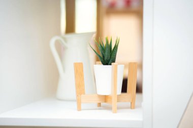 Small decorative artificial interior flowers in pots stand on miniature chairs on a shelf