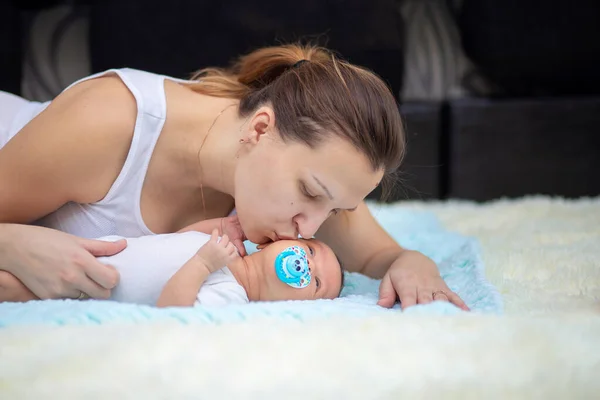 A young mother kisses her newborn baby. Baby sucks pacifier — Stock Photo, Image