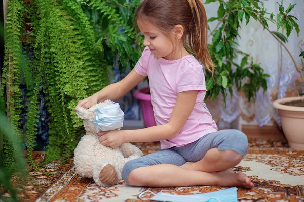 Chica Pone Una Máscara Médica Osito Peluche Sentado Casa Suelo — Foto de Stock