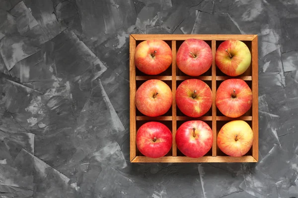 Red apples in a wooden box with cells on a concrete surface