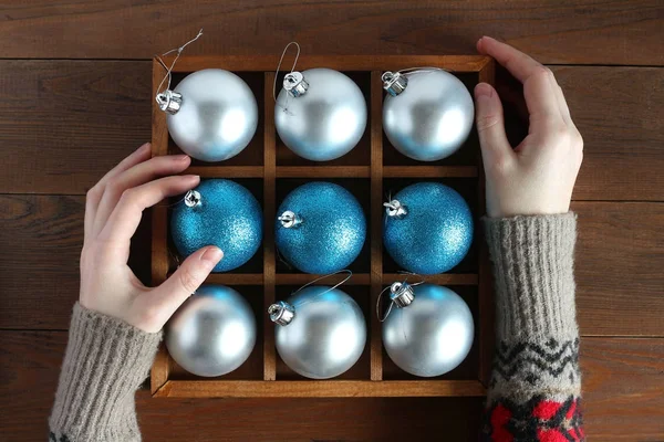 Female hands in woolen sweater holding wooden box with Christmas balls