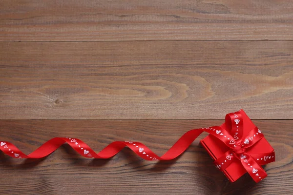 Red gift box with red tapes on a wooden background
