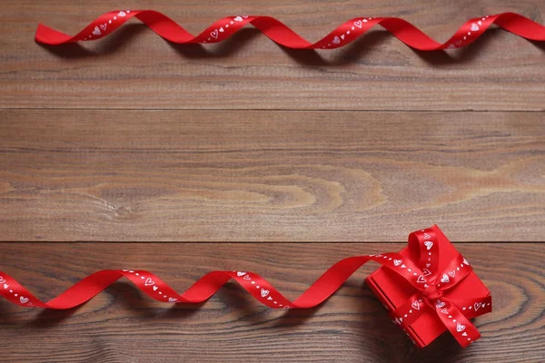 Red gift box with red tapes on a wooden background