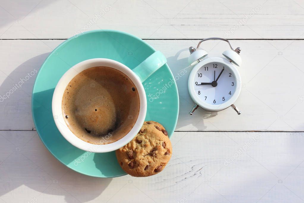 Coffee in a turquoise mug and cookies on a white table and the white alarm clock the top view