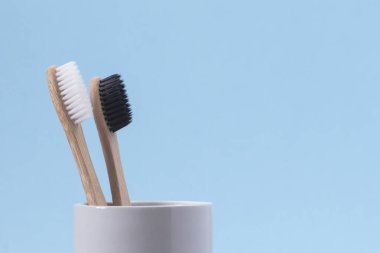 Mavi arka planda beyaz camlı beyaz ve siyah bambu diş fırçaları. Ekolojik ve sıfır atık kavramı