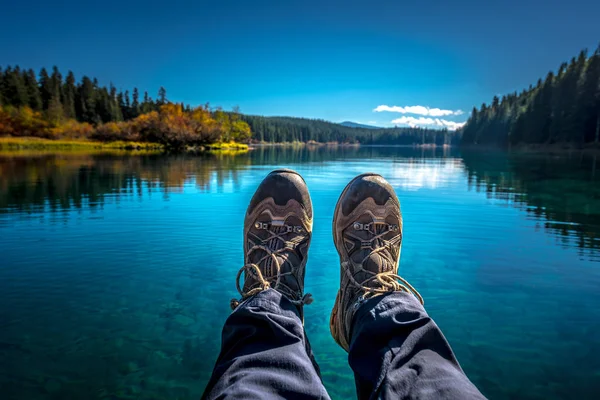 Female feet wearing hiking Boots resting over beautiful Clear Lake — Stock Photo, Image